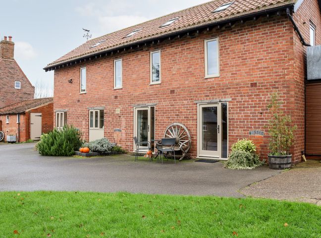 Exterior view of a brick building with multiple windows and doors surrounded by plants and outdoor furniture at The Granary in Askham