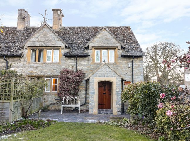 Stone cottage with a wooden door and two chimneys fronted by a lawn and plants at Bears Cottage in Bretforton near Broadway