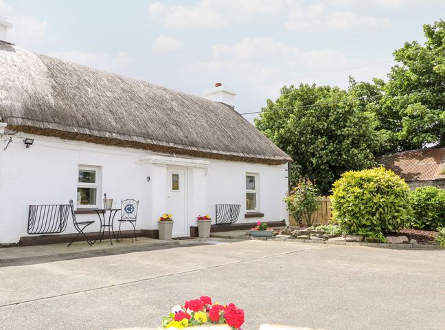 White thatched cottage with outdoor table and chairs near entrance and garden shrubs at Whispering Willows - The Thatch in Carndonagh County Donegal