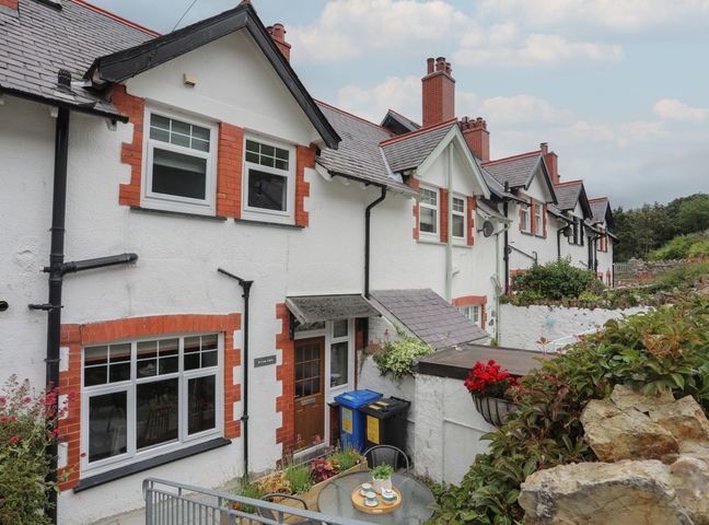 A row of white houses with red brick trim and a small outdoor seating area with plants at 2 Cae Glas in Dwygyfylchi near Penmaenmawr