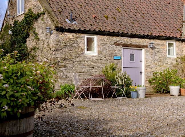 The exterior of a stone cottage with a tiled roof a purple door a small outdoor table and two chairs surrounded by plants and gravel at Pheasant Cottage Low Hagg Farm near Kirkbymoorside