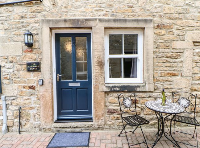 The entrance of a stone house with a blue door a window and an outdoor table and chairs at The Carriage House in Barnard Castle
