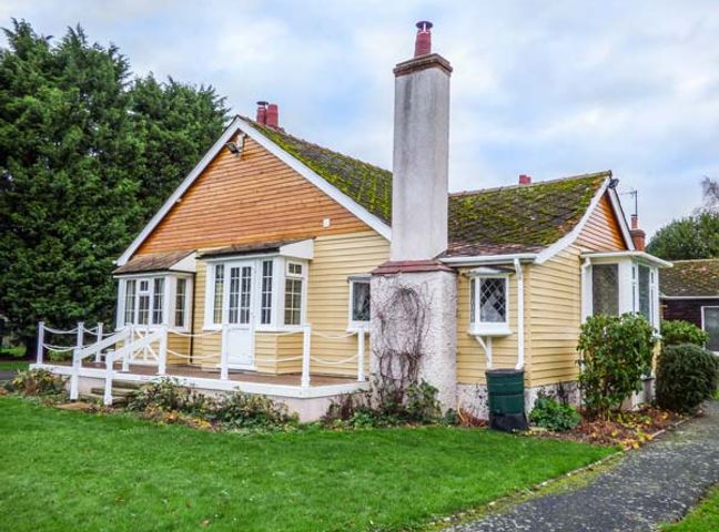 A single story house with a chimney a porch and surrounding plants at West Wing Le Chalet in Boston
