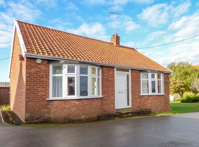 A brick bungalow with tiled roof and white front door with trees and garden area at Glenhaven Sweffling near Snape