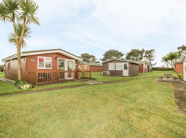 Several wooden cabins on a grassy area with palm trees and a picnic table at Tiggy Winkle in St Merryn near Padstow