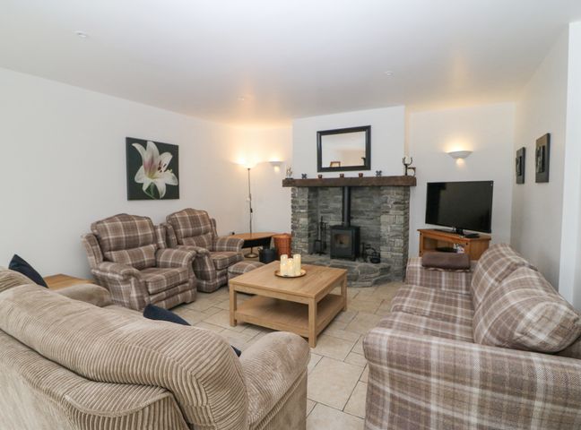 A living room with plaid armchairs sofas a stone fireplace wood stove a wooden coffee table and a television at Rock Lawn Cottage in Kealkill near Bantry County Cork