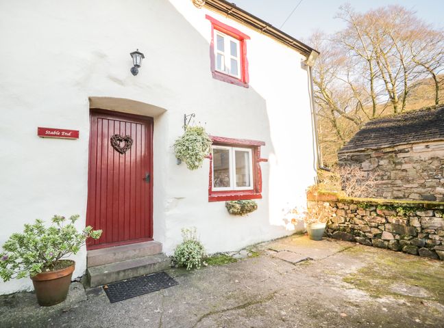 Exterior view of a white cottage with a red door and window frames with potted plants and stone wall Stable End Cottage Nether Wasdale near Gosforth