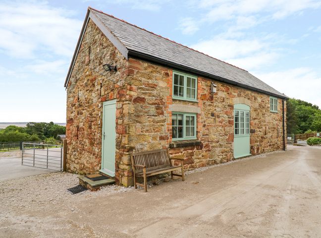 A stone exterior cottage with light green doors and windows and a wooden bench outside Plas Tirion Cottage Mostyn near Holywell