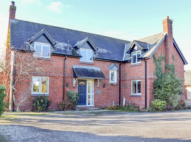 A brick house with a blue door and multiple windows surrounded by some plants and trees at Manor Wood in Farndon