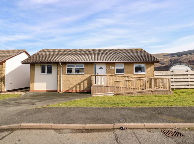 A single story house with a tiled roof a wooden ramp and a small front lawn at Sealyons in Fairbourne near Dolgellau
