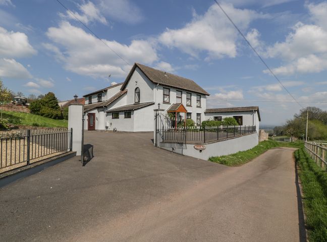 A white two story house with a tiled roof and gated driveway beside a country road at Moors Farm in Littledean