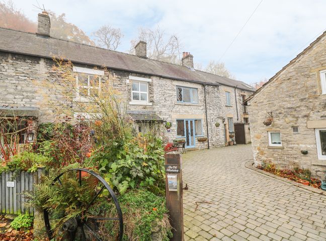 A stone building with blue framed windows and doors beside a paved courtyard with plants and flowers at Laburnum Cottage in Castleton