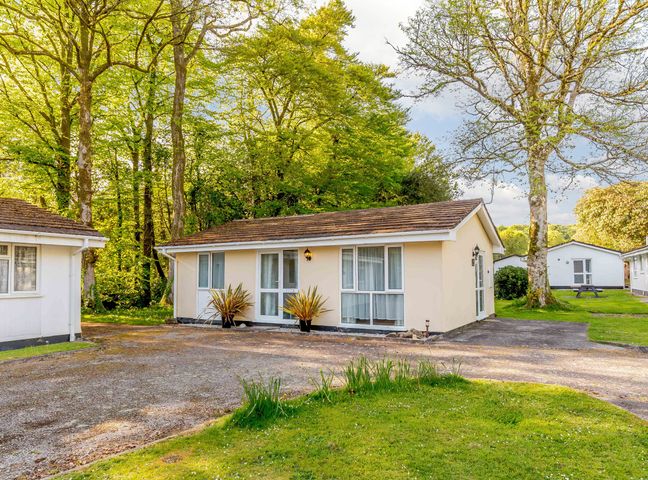 A single-story cottage with large windows and plants outside surrounded by trees and grass at Brook Cottage Rosecraddoc Lodge near Liskeard