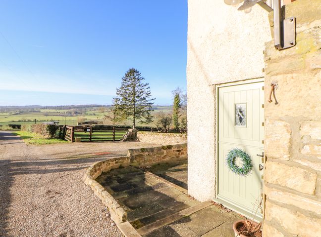 An exterior view of a building entrance with a light green door and a wreath next to a gravel driveway and wooden gates at The Stable Sedbury Park Farm in Gilling West near Richmond