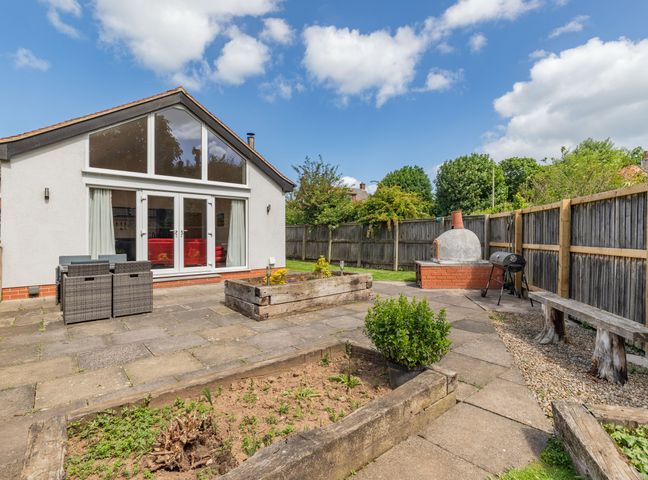 A backyard patio with a table and chairs a brick oven a charcoal grill raised garden beds and a bench at Hawthornden in Filey