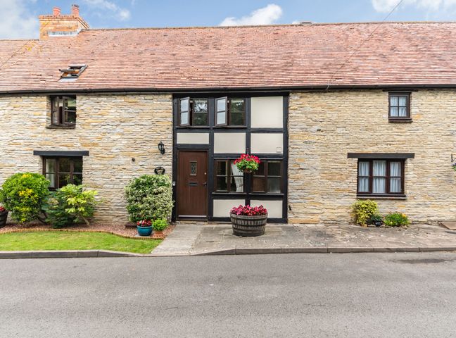The exterior of a stone house with a wooden door windows and flower pots at West End Barn in Cleeve Prior near Evesham