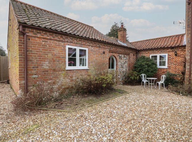A gravel courtyard with a small white table and two chairs outside a brick building at The Annexe Fulmodestone near Fakenham