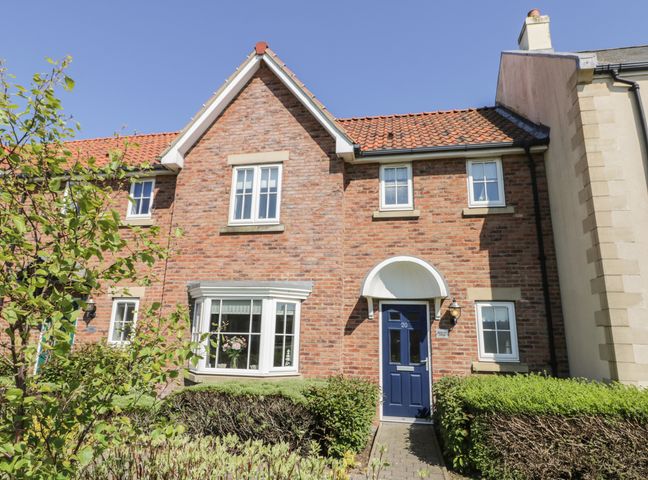 A brick house with a blue door and a bay window with bushes in front at White Rose Cottage The Bay near Filey