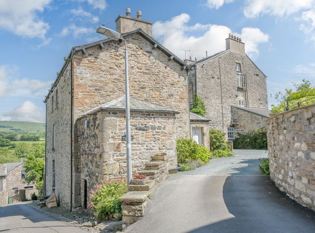 A stone house with a gated driveway and flowers by the entrance at Mill Brow Apartment in Kirkby Lonsdale