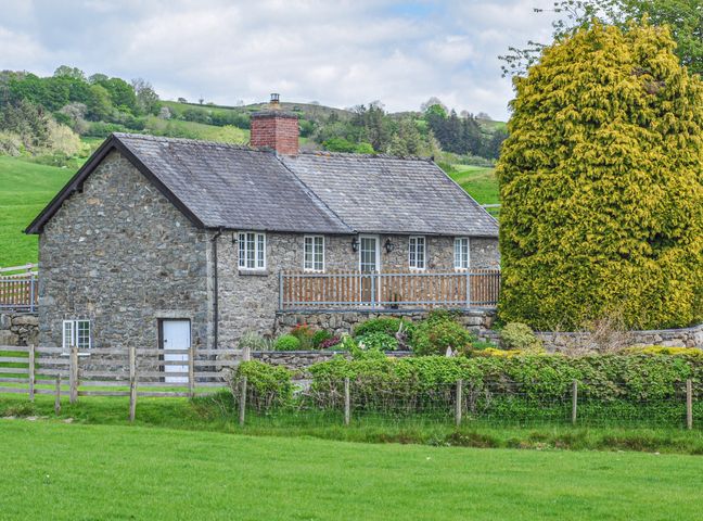 A stone house with a slate roof surrounded by green fields and a large tree at Hafan in Llanerfyl near Welshpool