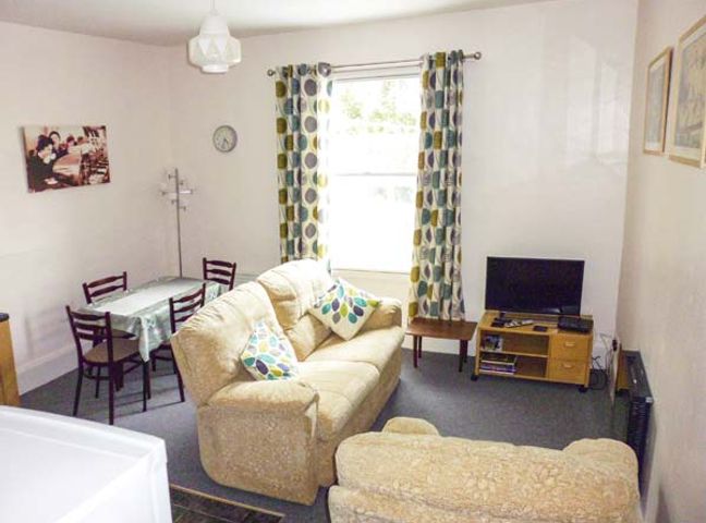 A living room with two beige sofas a dining table with four chairs and a television on a wooden stand at Harley Apartment in Bishop's Castle