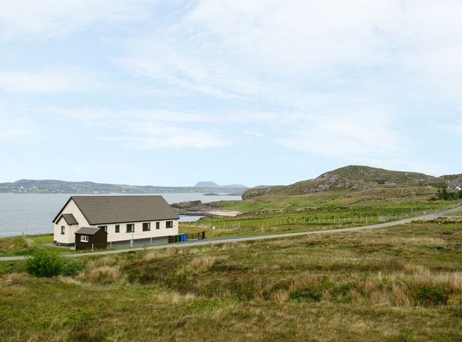 A house near a road with hills and water in the background at 1 Bayview Bungalow in Poolewe