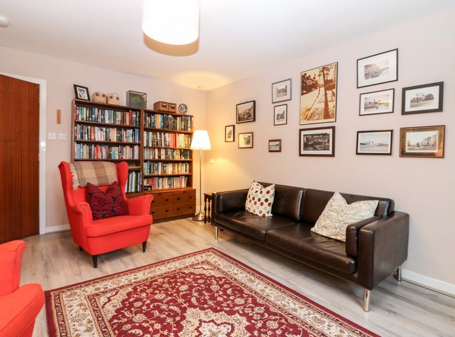 A living room with a leather sofa red armchair bookshelf and framed pictures on the wall at The Kate Kennedy Apartment in St Andrews