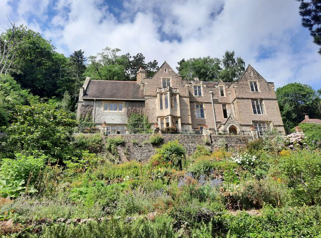 A large stone house with multiple windows on a hill surrounded by trees and a garden at Haslington House in Malvern