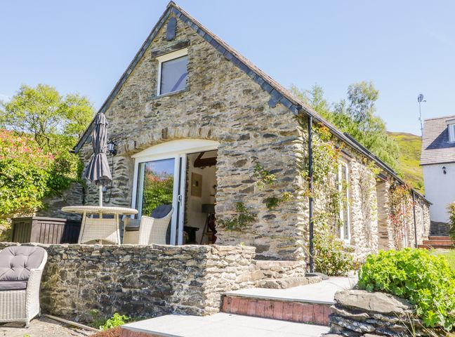 A stone cottage with outdoor seating and greenery at The Barn at Waen y Ffynnon in Ruthin