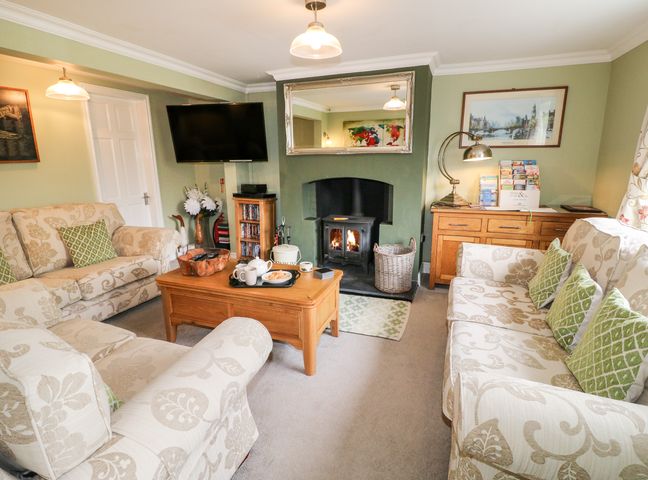 A living room with sofas a coffee table a wood burning stove and a wall mounted television at Aditum Cottage in East Barkwith near Wragby
