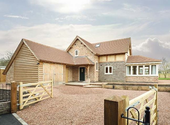 A brick and wood house with a gravel driveway and wooden gate at Rose Cottage in Winforton near Hay-on-Wye