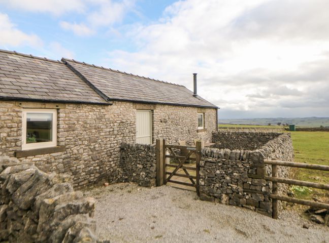 A stone barn with a gravel yard and wooden gate surrounded by dry stone walls at Five Wells Barn in Chelmorton near Buxton