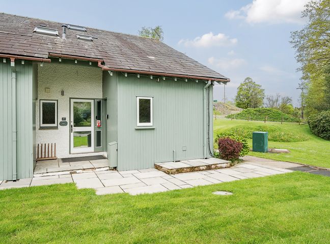 The exterior of a green cottage with a stone tiled pathway and a grassy lawn at Yew - Woodland Cottages in Bowness-On-Windermere