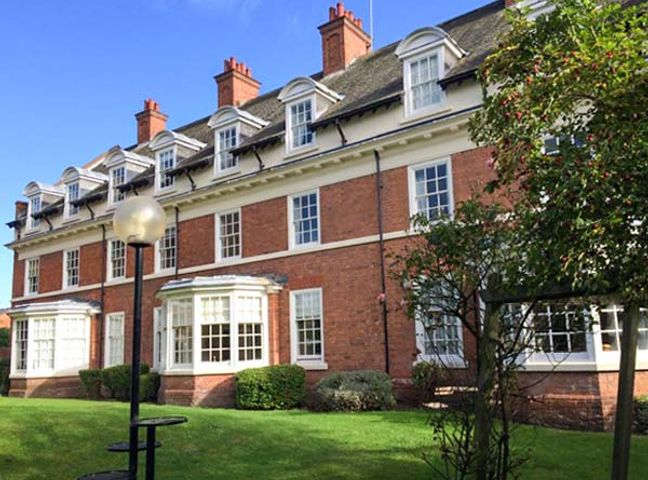 A brick building with multiple white windows and dormers surrounded by grass and bushes at The Feversham in York