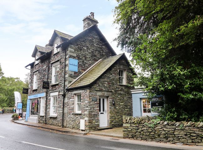A stone building with blue signs and shop windows on a street corner surrounded by trees at Shepherd's Crook in Grasmere