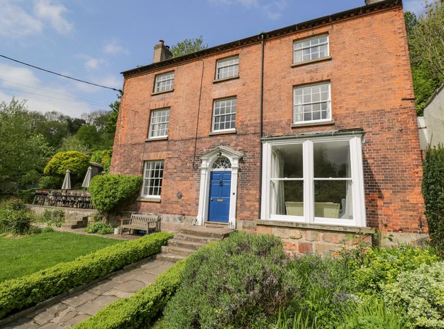 A brick house with a blue front door surrounded by bushes and a garden with a stone pathway at Viaduct House in Lydbrook