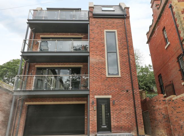 A modern three-story brick building with glass balconies and a black garage door at The Office Gardens Apartment 1 in Whitby