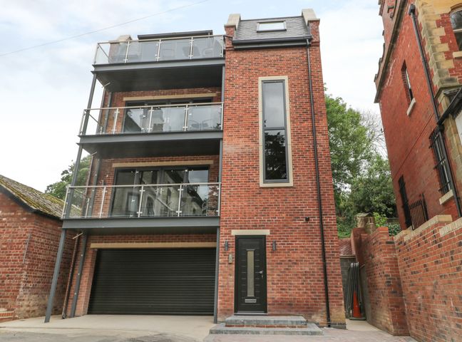 A multi-story brick building with glass balconies and a black garage door at The Office Gardens Apartment 3 in Whitby