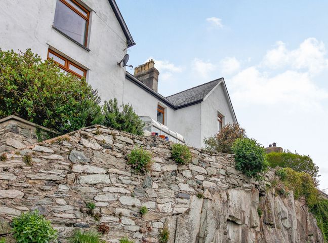 A white building with a stone wall and shrubs in front at Pen Y Graig in Talysarn