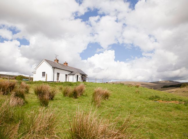 A white house with chimneys on a grassy hill under a partly cloudy sky at Shepherds Retreat in Gortin