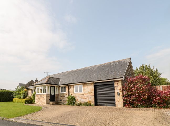 A single-story stone house with a black door driveway and plants at The Croft in Longhoughton near Alnwick