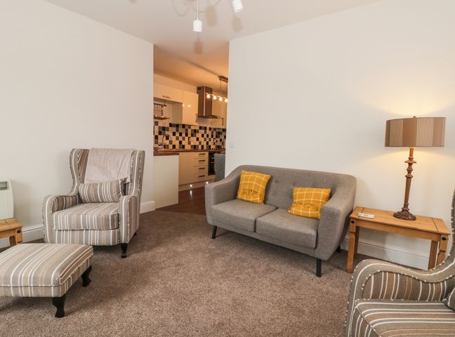 A living room with striped armchairs a gray sofa with yellow cushions a wooden side table and a lamp at Station View in Pickering
