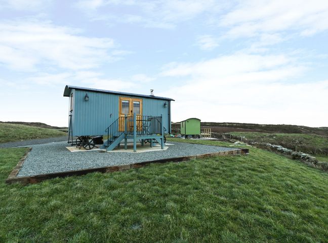 An outdoor grassy area with two small shepherd huts on gravel pads at Llety'r Bugail in Holyhead