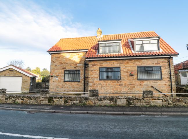 A stone house with a tiled roof and three windows facing the street with a stone wall in front at Avon Croft Cottage in Hawsker near Whitby and Robin Hoods Bay