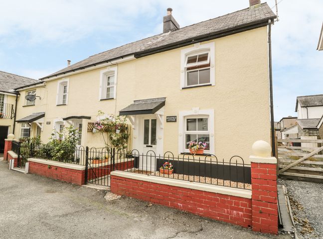 A yellow cottage with white framed windows and a small garden area at Brickfield Cottage in Machynlleth