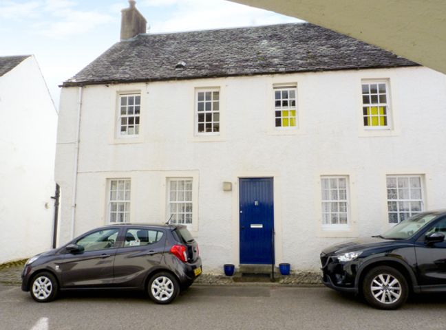 A white two-story house with a blue door and six windows with two cars parked in front at 8 Cathedral Street in Dunkeld