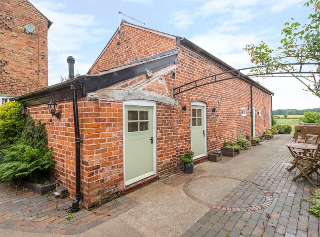 A brick building with two green doors and an outdoor seating area at The Dairy in Tarporley