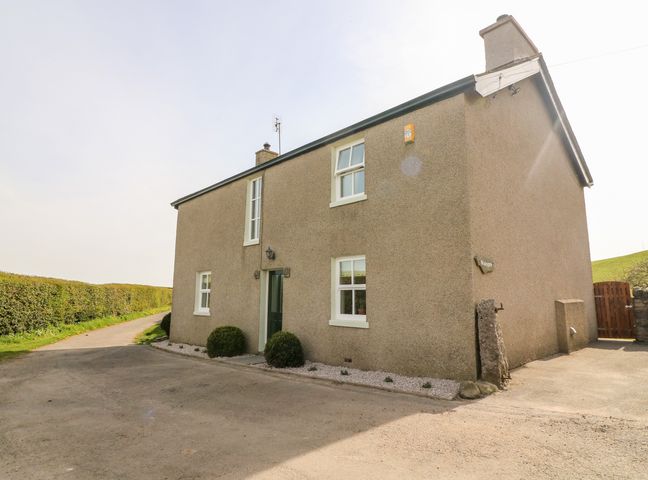 A two story house with a gravel pathway and bushes next to a road at Waingate Cottage in Flookburgh