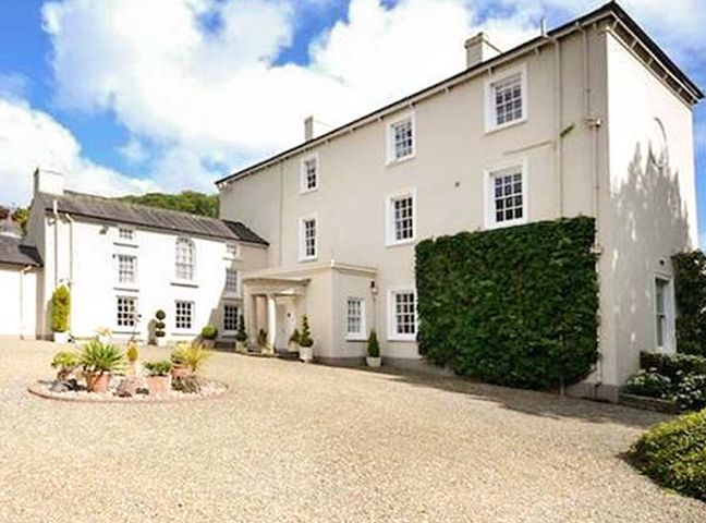 A large white multi-story house with several windows and a green ivy wall by a gravel driveway at Rhydlandgoed Stepaside near Saundersfoot