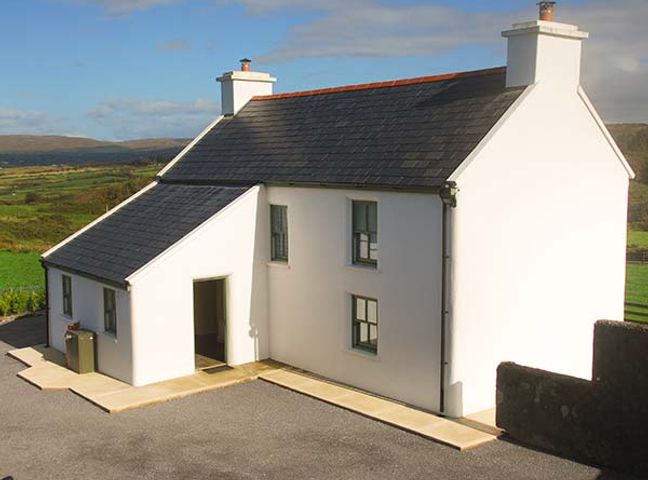 A white farmhouse with black roof and chimneys in a rural landscape at Nellies Farmhouse in Durrus near Bantry County Cork